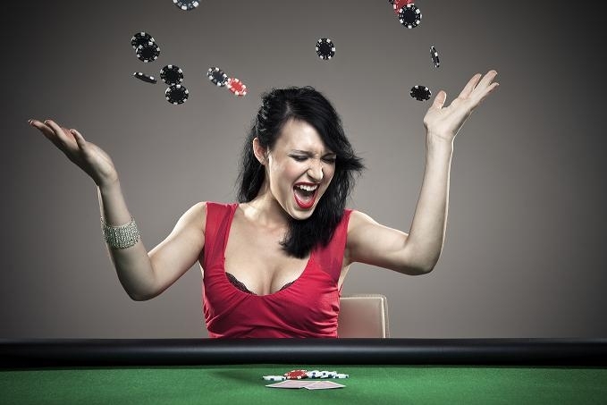 Девушка навеселе подбрасывает фишки, сидя за игровым столом