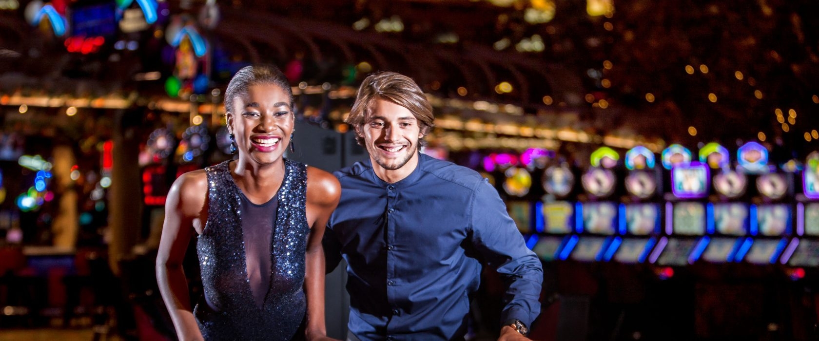 Сексуальная мулатка в обтягивающем платье и ее симпатичный парень веселятся в зале с игровыми автоматами