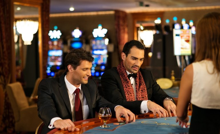 Смуглые мужчины в строгих костюмах распивают алкоголь за игрой в блэкджек в зале престижного казино