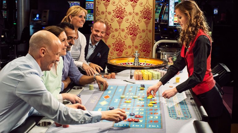 Молодая рыжеволосая девушка крупье ведет игру в рулетку для игроков, которые пришли в казино заработать денег и хорошо провести время
