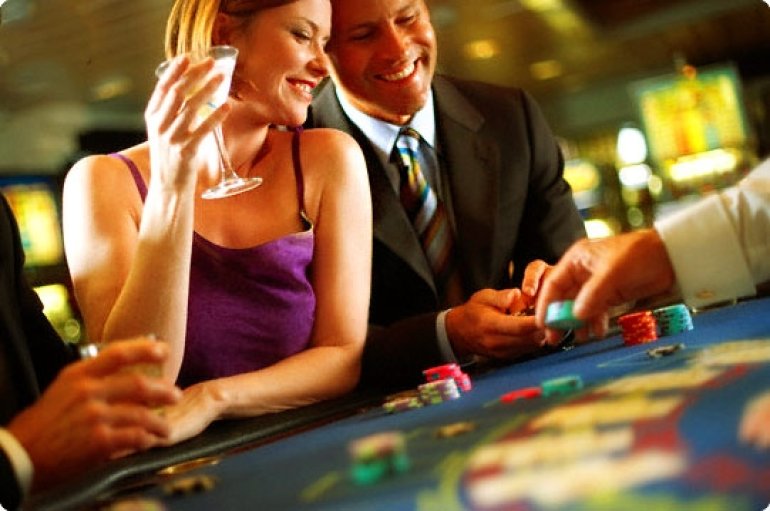 Пара приятно проводит время за игорным столом в казино, попивая алкогольные напитки