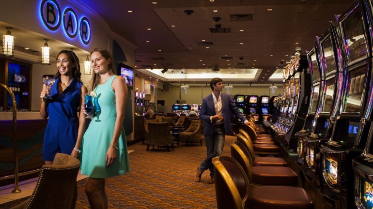 Две красотки в цветных мини-платьях распивают коктейли в зале с игровыми автоматами