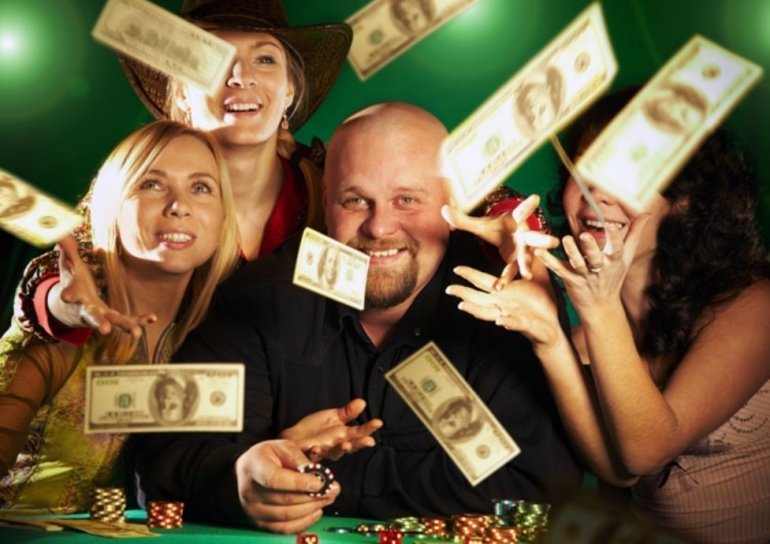 Мужчина и трое его прекрасных спутниц подбрасывают выигранные деньги, сидя за столом в казино