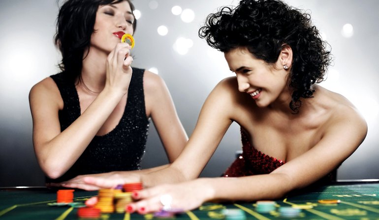 Две девушки сидят за игровым столом и счастливо улыбаются выиграв много фишек