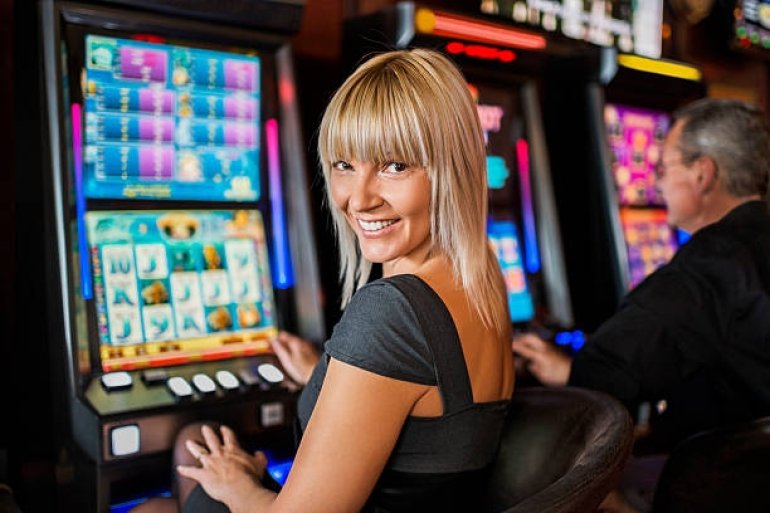 Симпатичная блондинка с улыбкой играет на автомате в казино