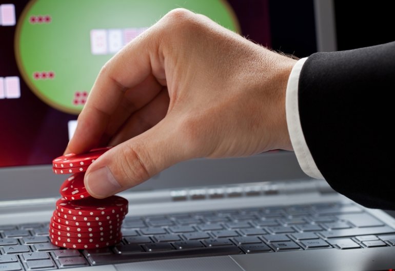 Рука игрока ставит фишки на класиатуру компьютера, а на мониторе открыт онлайн покер
