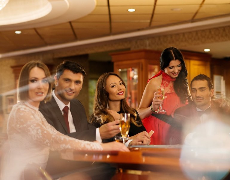 Элегантно одетые мужчины и женщины распивают шампанское за игорным столом в казино