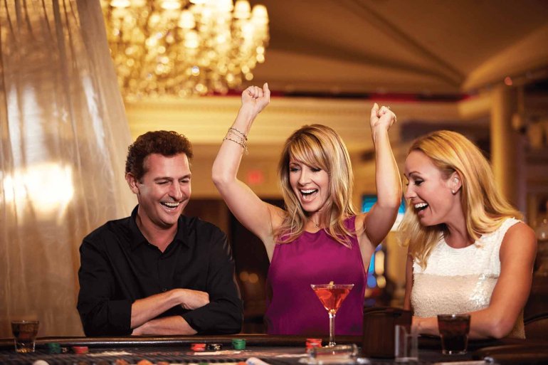 Молодой мужчина и две красотки играют в казино, распивая коктейли