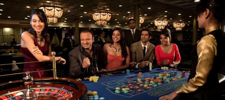 Женщины в вечерних платьях и мужчины в костюмах играют в рулетку в престижном казино в компании профессионального дилера