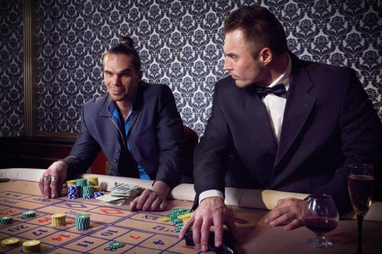 Два серьезных мужчины в деловых костюмах ведут азартную игру в вип-комнате, распивая виски