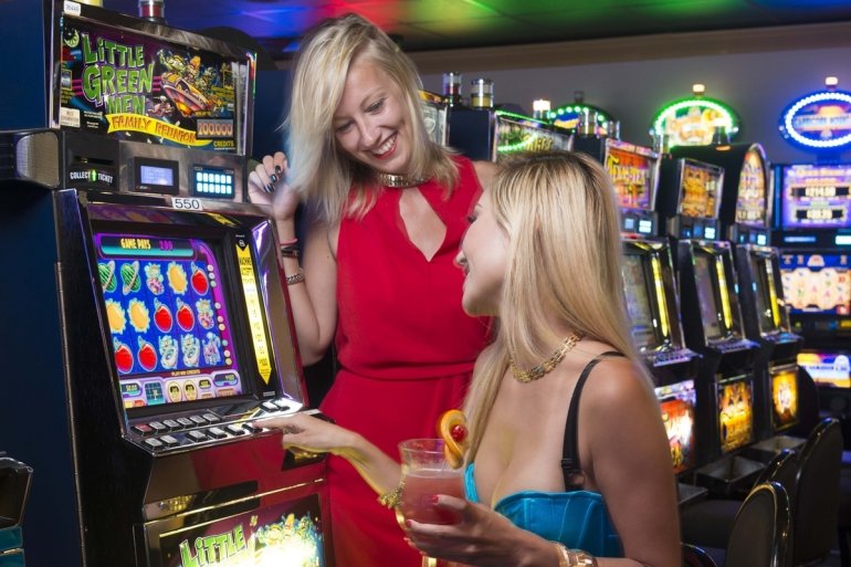 Две красотки блондинки в коктельных платьях за игрой на автомате