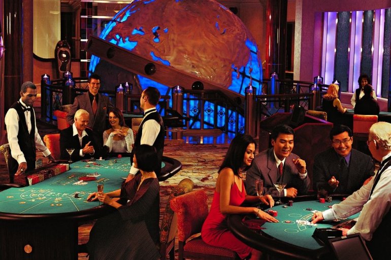 Зал казино со столома для разных игры, за которыми стоят крупье и сидят нарядные игроки