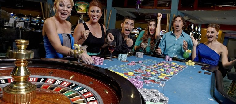 Веселые парни и девушки в красивой одежде распивают алкоголь и играют в рулетку в дорогом казино