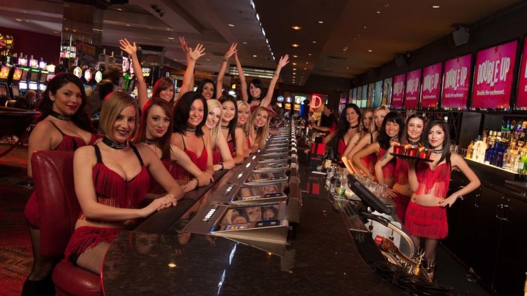 Секусуальные девушки дилеры в коротких красных платьях ждут игроков за столами в казино