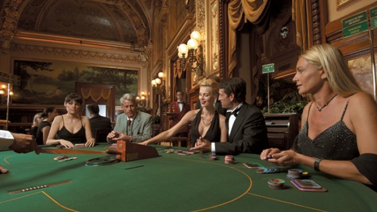 Красивые женщины в вечерних нарядах и мужчины в строгих костюмах играют в казино Monte Carlo в Монако
