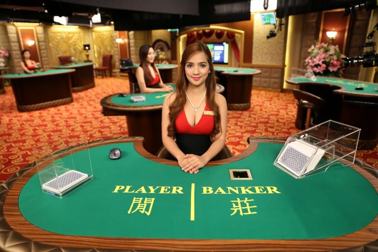 Пышногрудая азиатка со светлыми волосами ждет игроков за столом для баккара