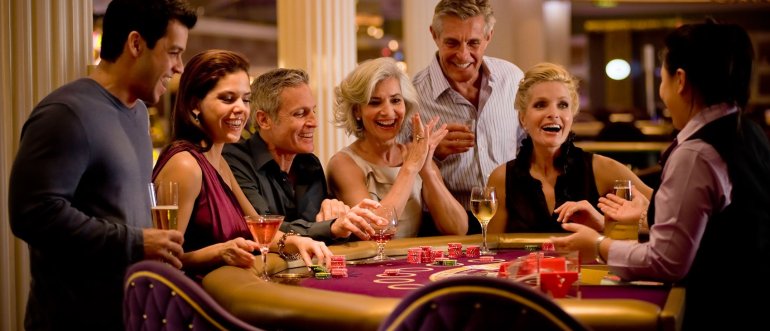 Мужчины и женщины распивают коктейли за игрой в блэкджек в зале дорогого казино