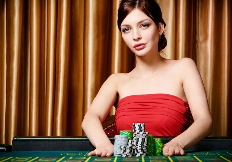 Привлекательная девушка в обтягивающем красном платье позирует, сидя за столом для игры в рулетку