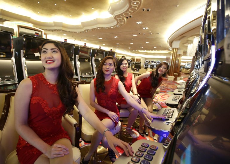 Четверо миниатюрных сексуальных азиаток в откровенных красных платьях сидят за игровыми автоматами в казино