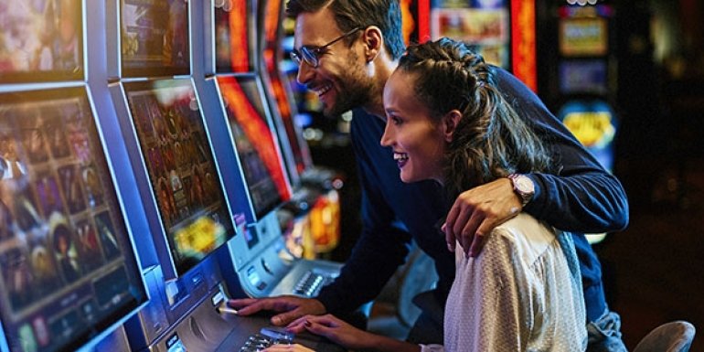 Парень с девушкой смеются и обнимаются, сидя за игровым автоматом в казино