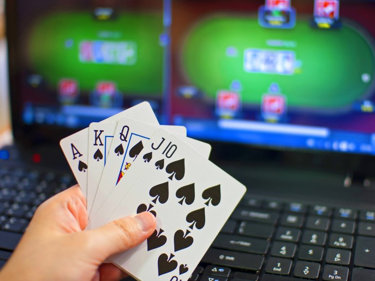 Карты в руках игрока, а на заднем фоне два экрана с виртуальным покером