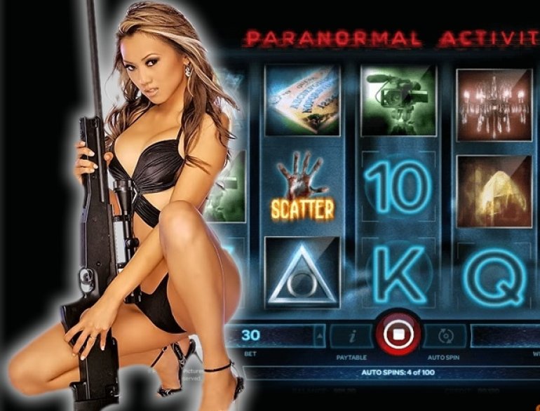 Сексуальная красотка в черном кожаном купальнике с винтовкой в руках позирует на фоне слота Paranormal activity
