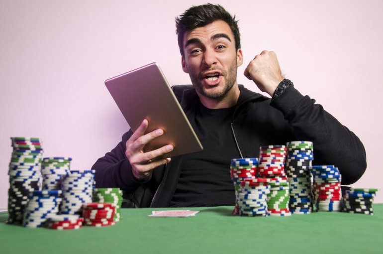 Мужчина восточной внешности сидит за столом для игры в покер с планшетом в руках