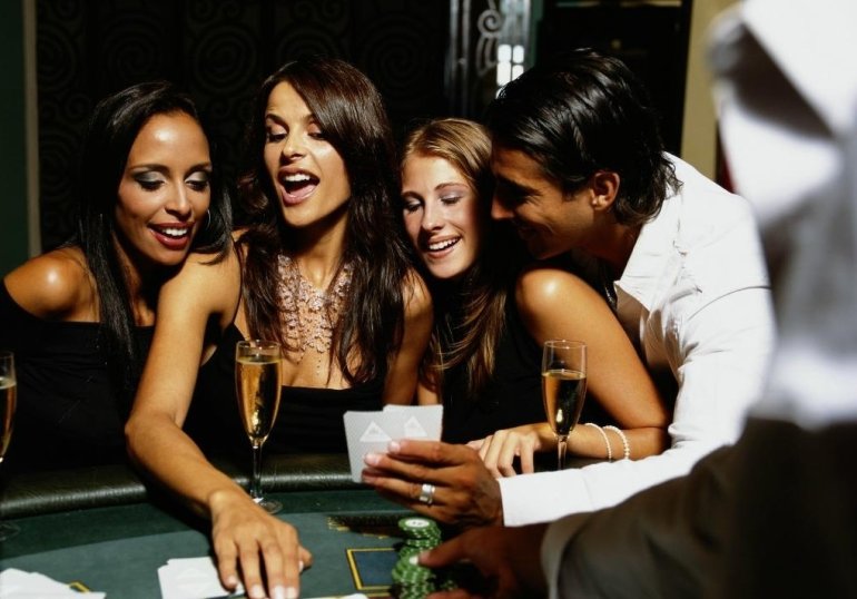 Три красотки распивают щампанское за игрой в казино, а симпатичный молодой мужчина нашептывает одной из них правильные варианты ходов