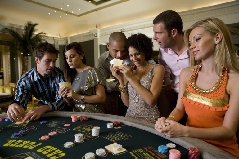Мужчины и женщины перешептываются, стоя у стола для покера с картами в руках