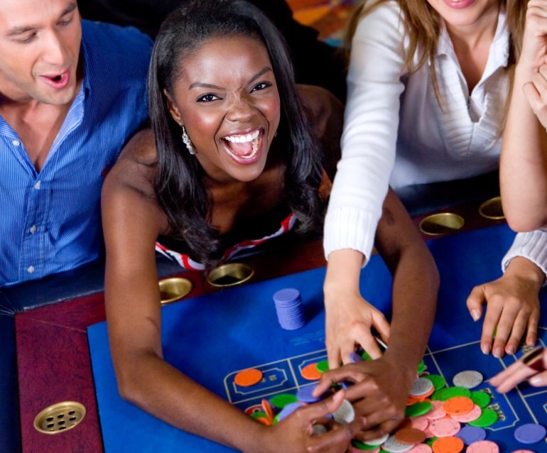 Азартная темнокожая девушка сгребает выигранные фишки со стола для рулетки